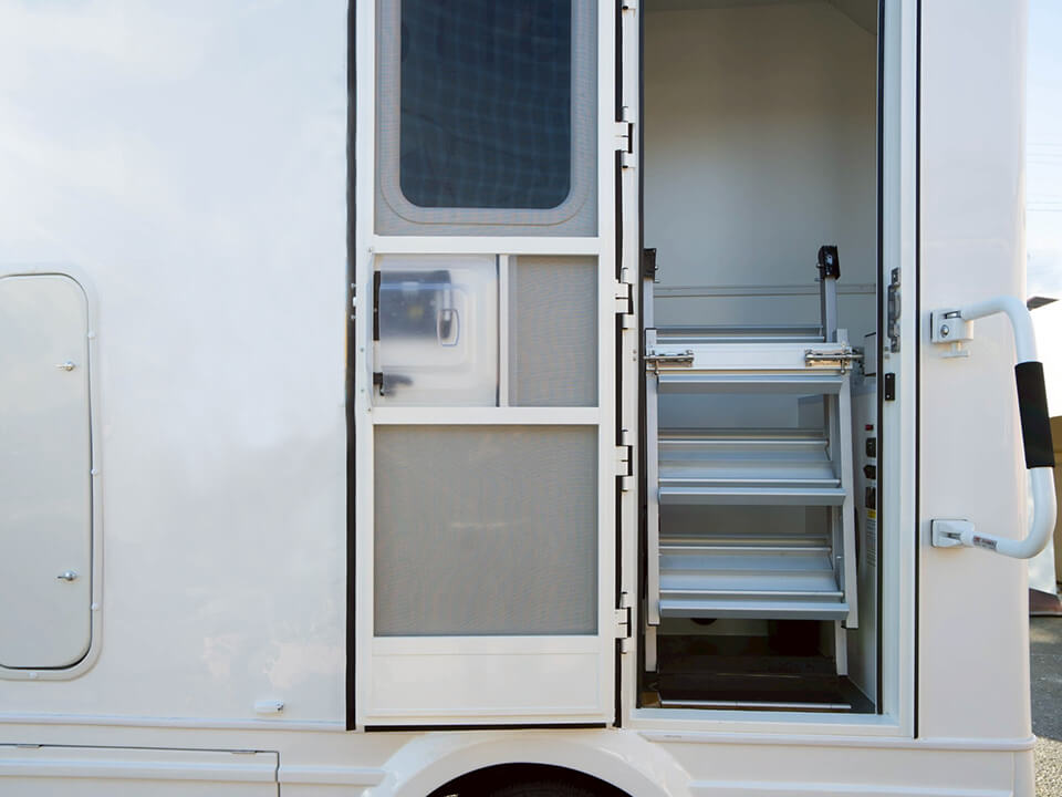 トイレカーの入り口に設置された折りたたみ式のアルミステップ（階段）と手すり