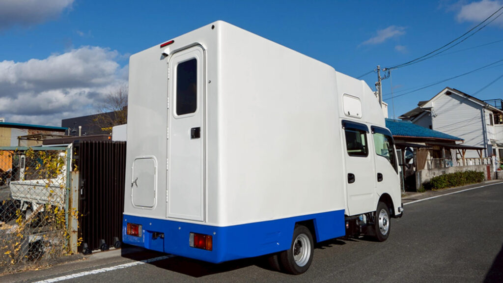 路上に停車したヴィオン製の白と青のツートンカラーの自走式トイレカー。